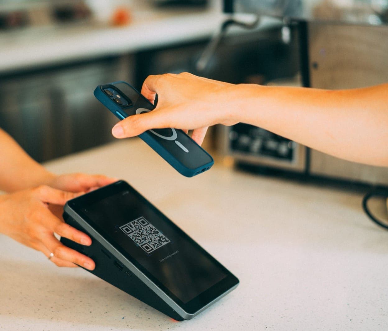 À la caisse, un client approche son téléphone d'un écran qui affiche un QR Code.